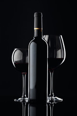 Bottle and glasses of red wine on a black background.