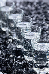 Damp glasses of vodka with ice on a black reflective background.