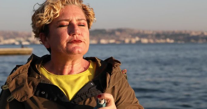 Woman seated on a park bench taking asthma treatment with inhaler