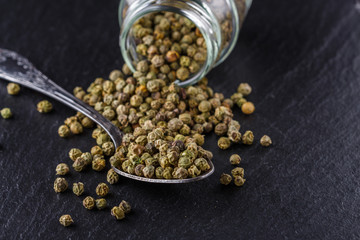 green peppercorns on dark slate stone background