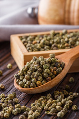 green peppercorns in wooden scoop on rustic background