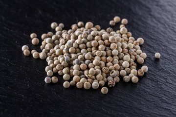 white peppercorns on dark slate stone background