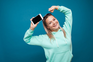 Stylish trendy hipster girl in the blue hoodie with the hood uses a smartphone.