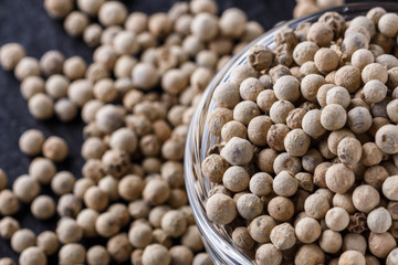 white peppercorns in glass bowl on stone background
