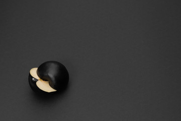 Two halves of a black apple on the matte black background. Minimal style. Conceptual minimalist...
