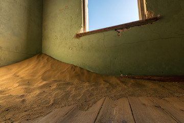 A close up photograph of an old, broken window, with desert sand piling in the corner of an abandoned house, taken in the ghost town of Kolmanskop, Namibia.