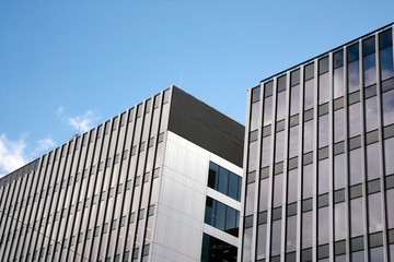 Modern curtain wall made of glass and steel. Blue sky and clouds reflected in windows of modern office building. 