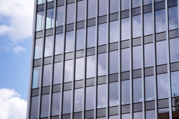 Modern curtain wall made of glass and steel. Blue sky and clouds reflected in windows of modern office building. 