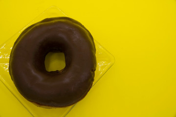 Chocolate donut on a yellow background, overhead photo