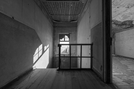 A black and white photograph inside an abandoned house at the top of a stairway, taken in the ghost town of Kolmanskop, Namibia.