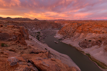 A beautiful pink sunset landscape view of the Augrabies Falls Gorge, mountains and river in South Africa, taken on a stormy cloudy golden evening. - Powered by Adobe