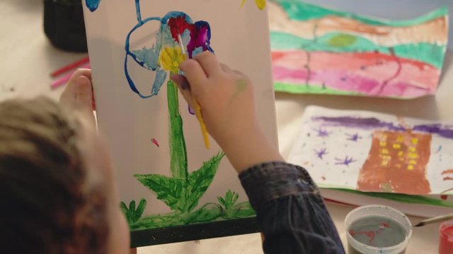 Kids interest group. Art class. Girl painting colorful flower on easel.