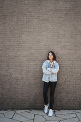 Vertical portrait of happy, satisfied good-looking young queer girl in denim jacket, glasses, lean on brick wall and chilling under spring warm sun, good day for walking enjoying weekend