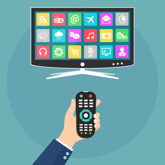 Hand holding remote control and smart tv with apps icons on screen