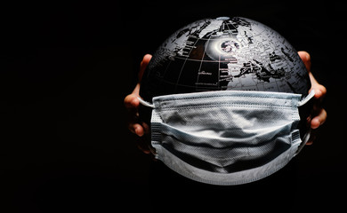 Hands of little child holding globe sphere, planet map covered with medical protective mask isolated on black background. Concept of COVID-19 pandemic infection