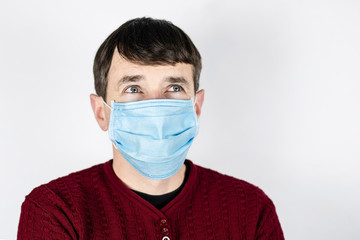 A man in a medical mask on a light background looks up because he is looking for God to avoid getting a dangerous virus. A man is afraid of a global pandemic