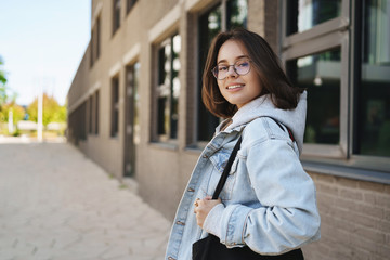 Outdoor portrait of modern young queer girl, female student in glasses and denim jacket, going home...