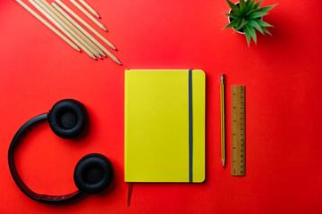 Milan / Italy - March 2020: Flat lay, notebook yellow with various objects (pencils, headphones, ruler) with red background