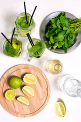 Making a cold summer mojito drink with lime, mint leaves, straw, ice cubes, soda and rum on a white background.
