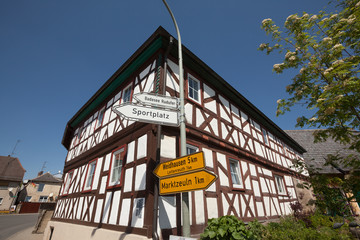 Sign post with 2 white and 2 yellow signs in front of a half-timbered house in Schwürbitz, Michelau, Franconia, Bavaria, Germany.