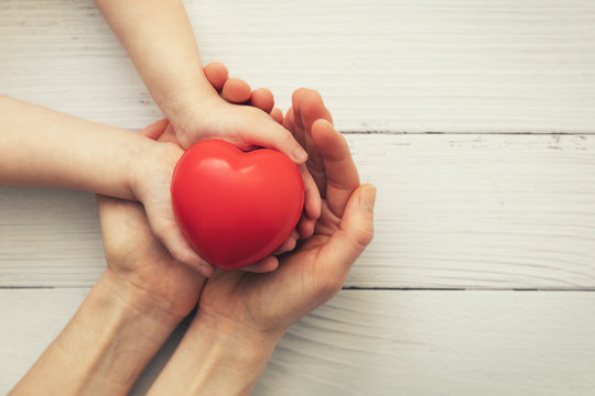 Red Heart In Child And Mother Hands On White Wooden Background. Concept Of Love, Charity, Empathy