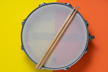 Drum stick and drum on yellow and orange color table background, top view, music concept