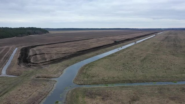 Two parts of field-before and after plowing, and working tractor in background. Irrigation canal near the field. An open channel for watering fields. Cloudy day. Agricultural landscape from the air.