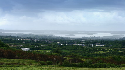 Fototapeta na wymiar summer landscape view over lough Corrib with hazy sky and clouds over rolling hills and green forests, Galway, Ireland