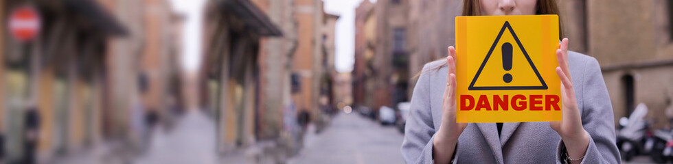  Coronavirus. Girl holds a yellow sign in her hands with the text Danger. The concept of pandemic and infectious diseases worldwide. Girl on the street of Italy. Copy space . Banner. long format. Blur