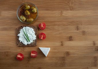 Sliced rye bread with cottage cheese and vegetables on wooden table