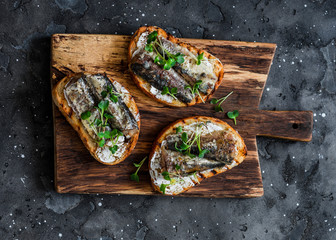 Grilled bread sardines micro greens sandwiches on a rustic cutting board on a dark background, top...