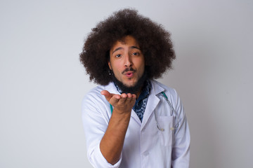 Cute appealing doctor male blows kiss at camera, demonstrates love to boyfriend or says goodbye on distance, isolated over gray studio background.