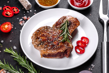 Fresh delicious juicy steak on the bones with vegetables and spices against a dark background