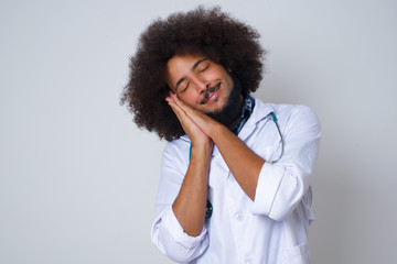 Relax time. Tired beautiful African American doctor with closed eyes leaning on palms as pillow pretending sleeping being exhausted seeing dreams standing against gray background. Sleeping gesture.