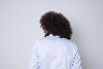 The back side view of a doctor man with afro hair standing against gray wall. Studio Shoot.