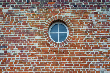 fen&ecirc;tre ronde avec croisillon dans un mur de briques.