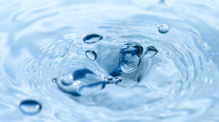 Water drops falling into Light Blue water and making ripples.