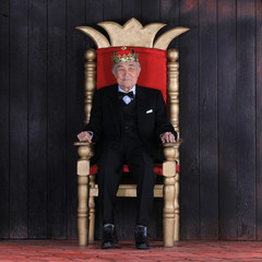 old king with a crown on the royal throne on a black background