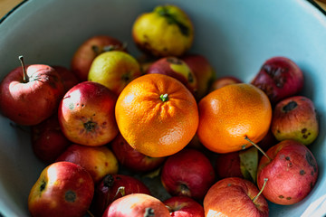 Bright juicy fruits, natural and natural fruits   with damage. Red apples and tangerines in a Cup   with sun rays