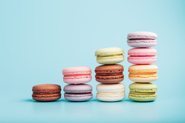 Macaroni cookies of different colors are arranged in the shape of pyramid steps on a blue background.