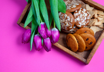A tray with cookies and pink tulips on a pink background. Round homemade cookies with almonds and lingonberries. Delicious pastries, snack. Flour product, food.