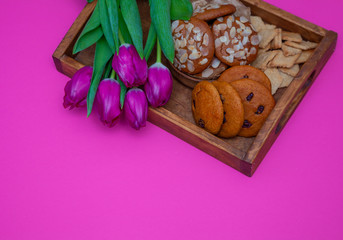 A tray with cookies and pink tulips on a pink background. Round homemade cookies with almonds and lingonberries. Delicious pastries, snack. Flour product, food.