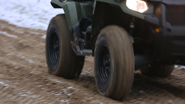 The wheels of an ATV drive through the sand. The ATV goes off-road, close-up. Wheel marks on wet sand. Off-road in the winter. ATV off road wheels.
