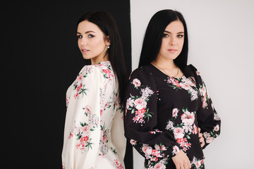 Two fashion brunette models in spring dresses posing in the studio. Black and white background