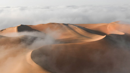 Fototapeta na wymiar Aerial view of a massive sand dune surrounded by winter morning fog cloud in Empty Quarter. Liwa desert, Abu Dhabi, United Arab Emirates.