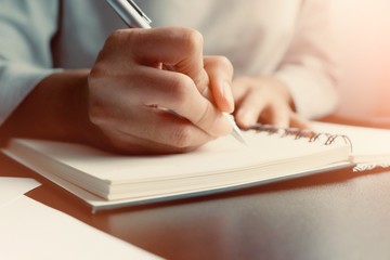 The hand of a young woman writing note of the warning message, details, things to do or preparation information of report with a bronze pen onto the book used eye preservation paper, green cover page