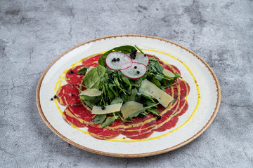 Gourmet snack: beef carpaccio with a bunch of spinach and parmesan slices