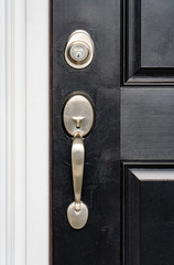 Close-up view of brand new nickel single cylinder front door handle set and matching lock deadbolt  on a black wooden door