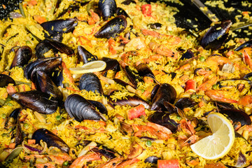 Close up of large portion of traditional Spanish paella dish freshly being cooked with seafood and rice in a frying pan at a street food festival, ready to eat seafood, side view, selective focus