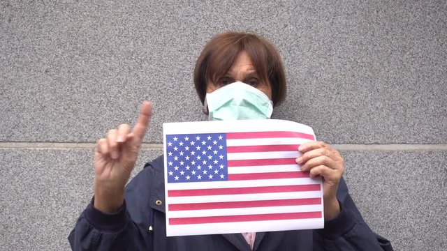 Europe - Italy - Milan - 70 year old lady with  mask on face to protect herself from the global epidemic of Novel Coronavirus n-cov 19 shows the flags of Usa America infected 